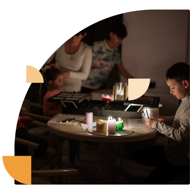Een tafel met brandende kaarsen en een gezin in het donker, een situatie die de gevolgen van een cyberaanval op de stroomvoorziening visualiseert.