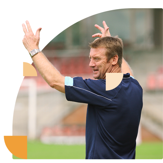 Trainer met opgeheven handen motiveert spelers tijdens een voetbalwedstrijd.